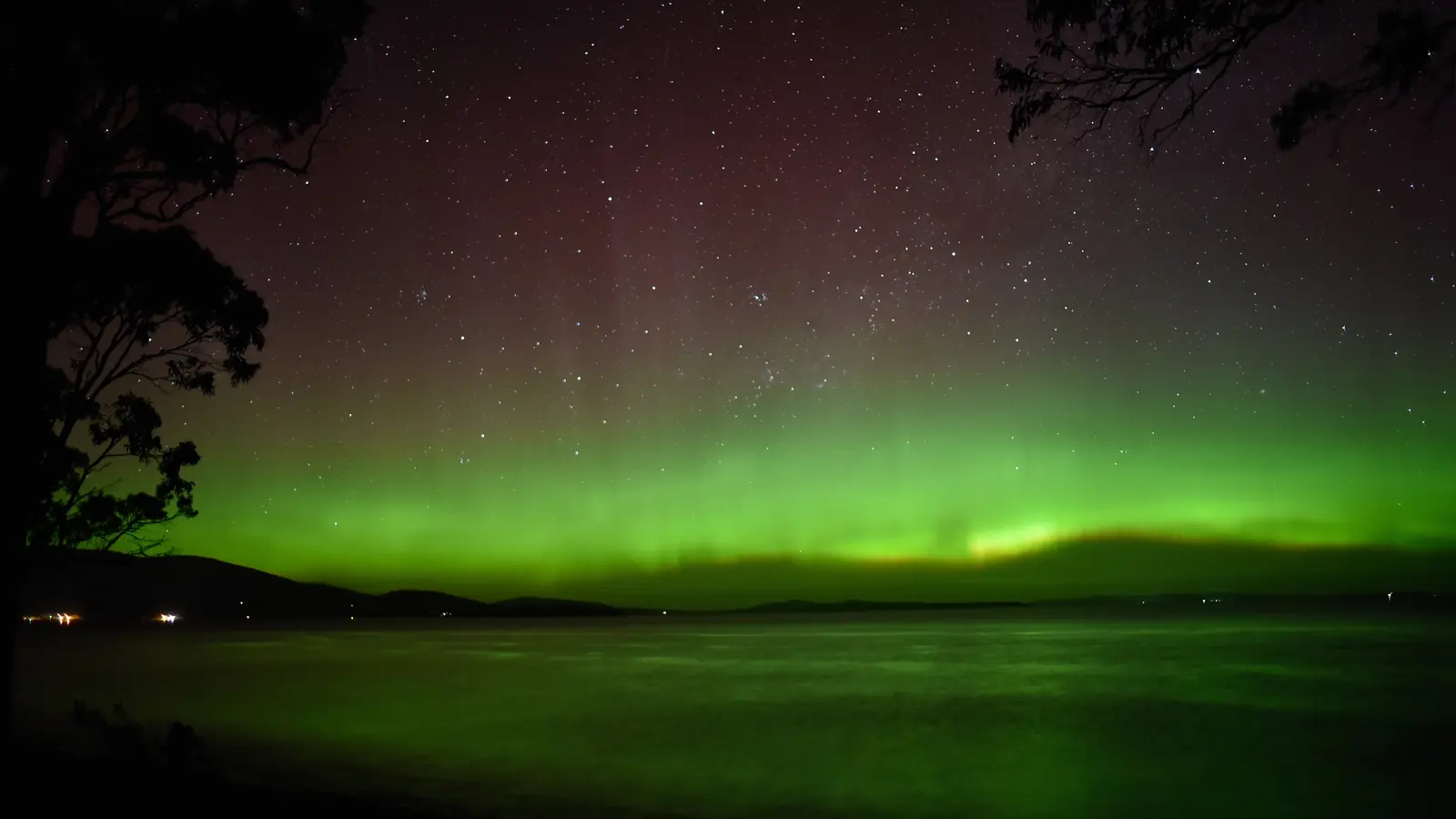 Aurora australis glowing green and red above calm southern water