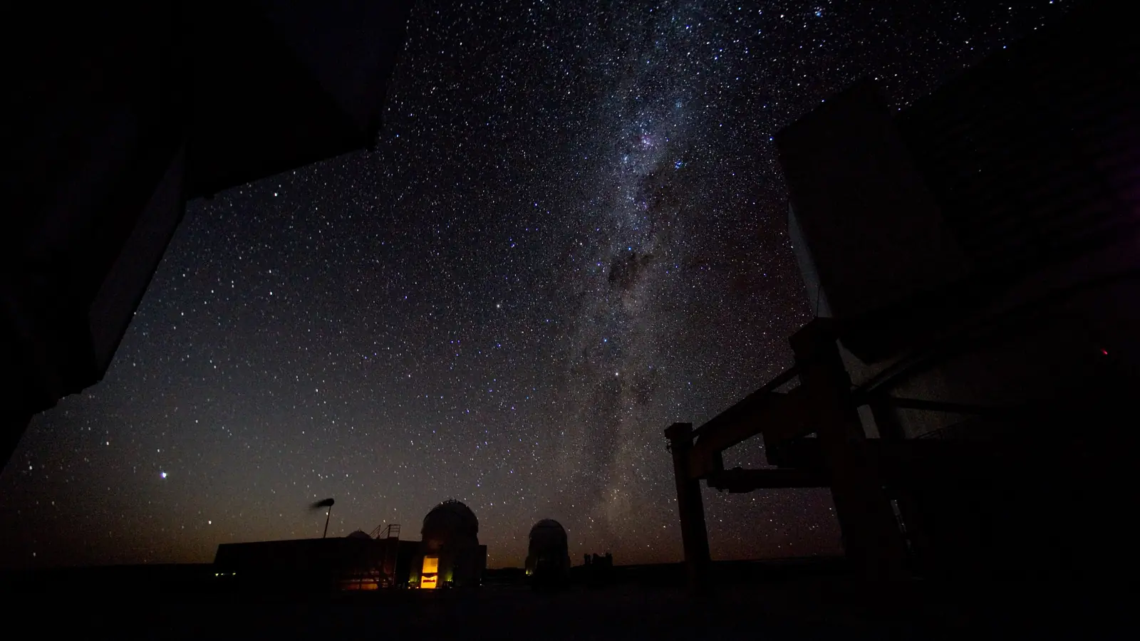 The Milky Way arching over telescope domes on a desert mountaintop